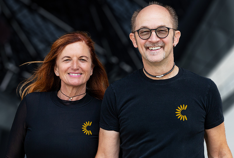 Claudia und Armin Kapser in schwarzen Shirts mit Firmenlogo lächeln in die Kamera.